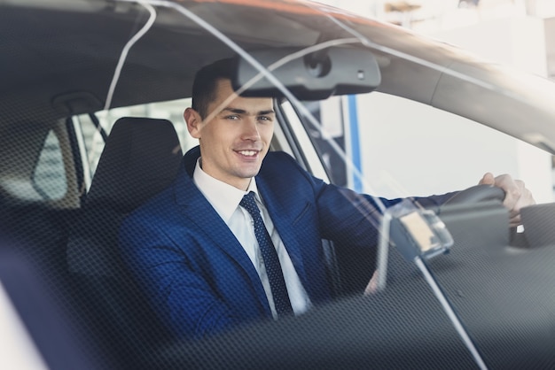 Young and happy businessman sitting in new car in showroom