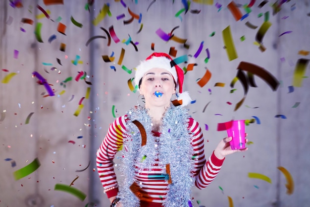 young happy casual business woman wearing a red hat and blowing party whistle while having new years confetti party in front of concrete wall