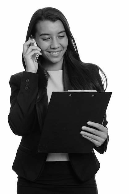 Young happy Caucasian businesswoman smiling and talking on mobile phone while reading on clipboard