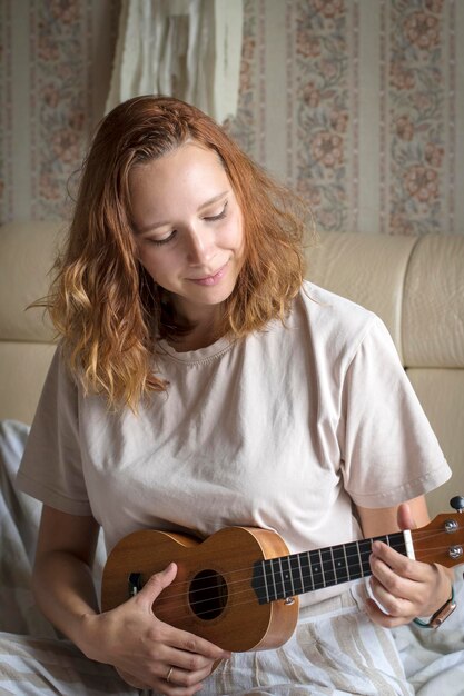 Young happy cheerful girl learning to play the ukulele portrait of a girl playing ukulele at home