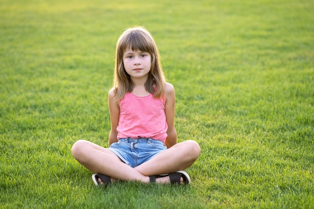 暖かい夏の日に緑の芝生の芝生に座って休んでいる若い幸せな子の女の子