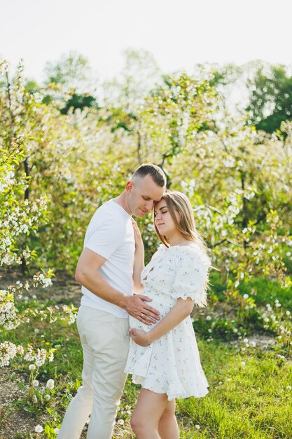 Молодая счастливая пара в ожидании беременности гуляет по цветущему саду Влюбленная пара среди цветущих яблонь