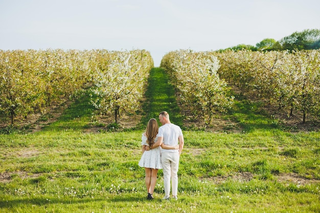 임신을 기대하는 젊은 행복한 부부는 꽃이 피는 정원을 걸어가며 꽃이 피는 사과나무에서 사랑하는 부부는