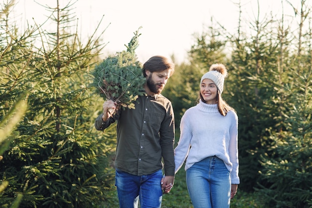 Молодая счастливая пара купила свежую елку на плантации, готовясь к праздникам. концепция счастливых зимних праздников.