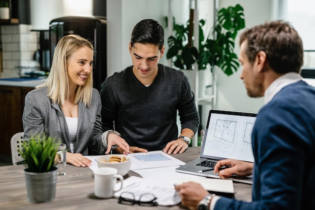 Young happy couple communicating with real estate agent while examining blueprints on a meeting