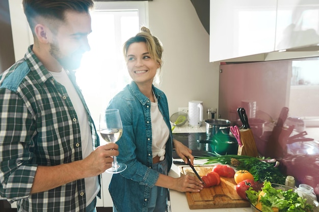 Photo young and happy couple cooking launch and drinking wine together in the kitchen