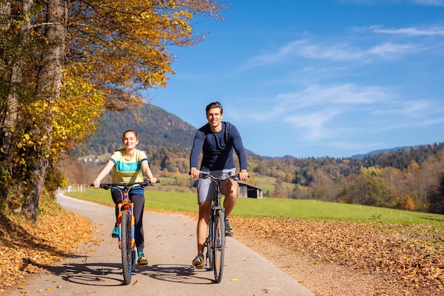 젊은 행복한 커플이 손을 잡고 재미있게 가을의 숲길을 따라 산 아래로 자전거를 타고