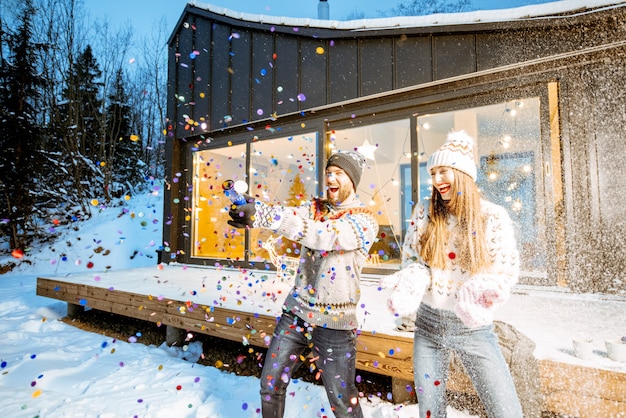 겨울 휴가를 축하하는 스웨터를 입은 젊은 행복한 커플이 산에 있는 아름다운 장식 집 앞에서