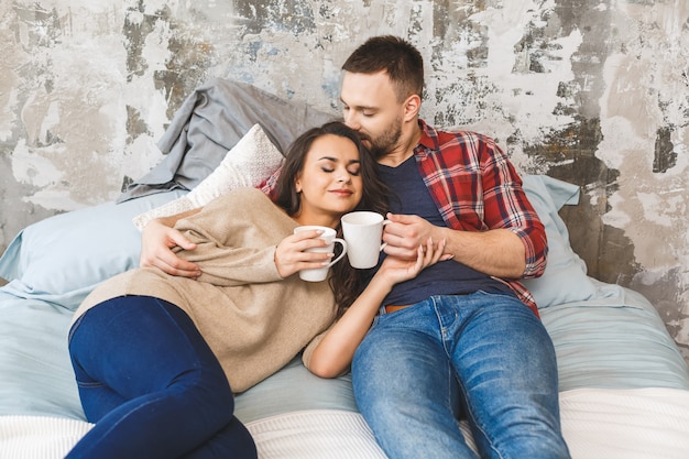 아침에 침대에서 커피 또는 차를 마시는 젊은 행복 한 커플.