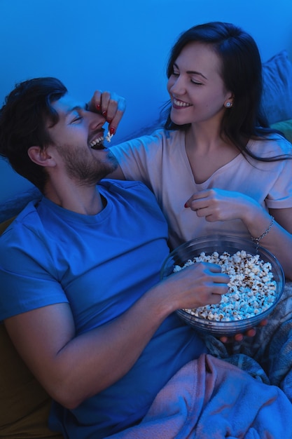 Молодая и счастливая пара ест попкорн и смотрит фильм