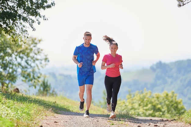 Foto giovane coppia felice che gode di uno stile di vita sano mentre fa jogging su una strada di campagna attraverso la bellissima foresta soleggiata, l'esercizio fisico e il concetto di fitness