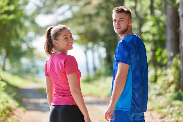 young happy couple enjoying in a healthy lifestyle while jogging on a country road through the beautiful sunny forest, exercise and fitness concept