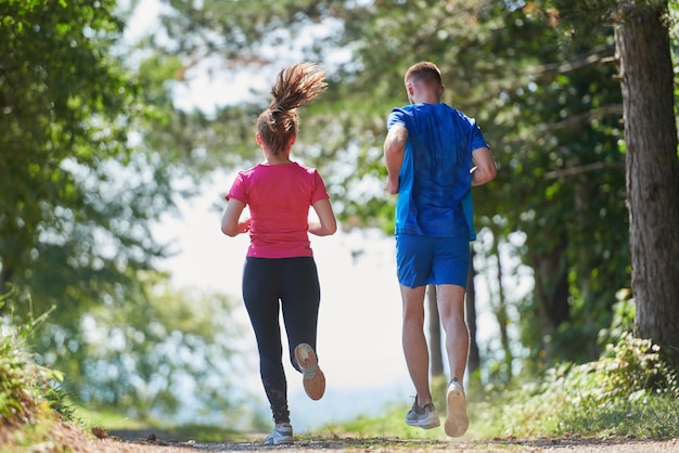 young happy couple enjoying in a healthy lifestyle while jogging on a country road through the beautiful sunny forest, exercise and fitness concept