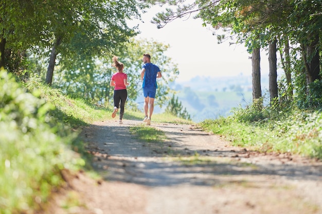 young happy couple enjoying in a healthy lifestyle while jogging on a country road through the beautiful sunny forest, exercise and fitness concept