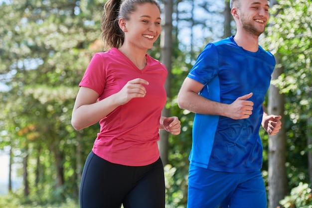 молодая счастливая пара наслаждается здоровым образом жизни во время пробежки по проселочной дороге через красивый солнечный лес, упражнения и фитнес-концепцию