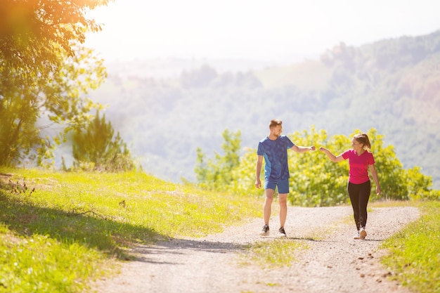 young happy couple enjoying in a healthy lifestyle while jogging on a country road through the beautiful sunny forest, exercise and fitness concept