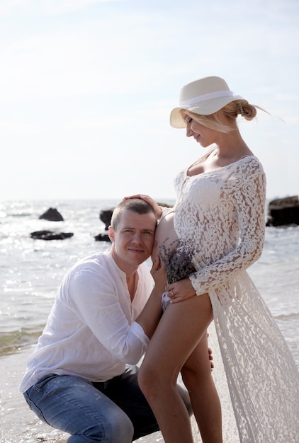 Young happy couple future parents near ocean, man listen new life in belly