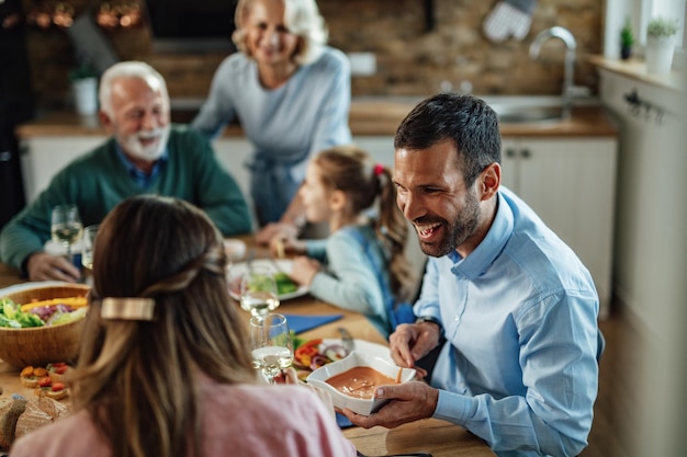 ダイニングルームで家族の昼食をとっている若い幸せなカップル。焦点は、男性が妻に食べ物を渡すことにあります。