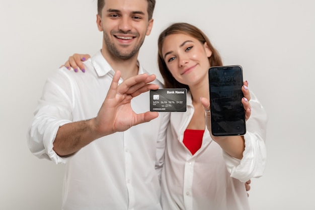 Photo young happy couple holding credit bank card using smartphone isolated on white background focus