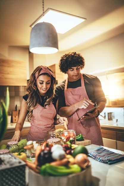 Фото Молодая счастливая пара наслаждается и готовит здоровую еду на своей кухне и читает рецепты на планшете.