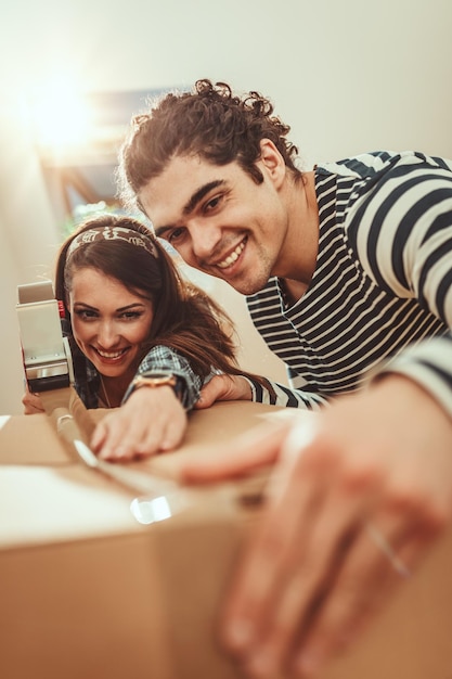 The young happy couple is moving into a new house. They are packing boxes with things to their new living room.