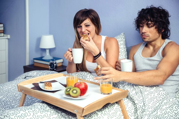 Foto giovane coppia felice innamorata che fa colazione a letto servita su un vassoio a casa. concetto di stile di vita domestico delle coppie.