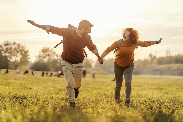 Young happy couple in love holding hands and running in nature. It's a beautiful sunny autumn day. Freedom.