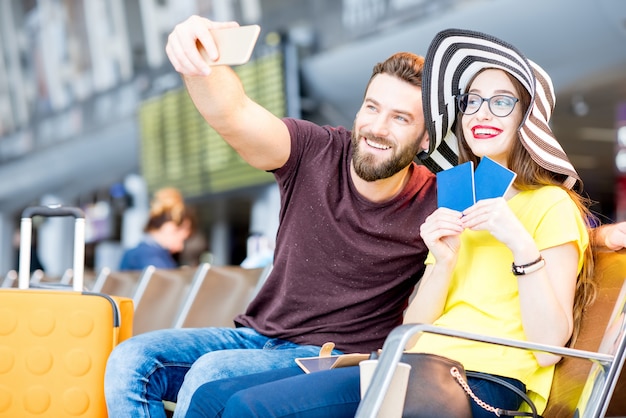 젊은 행복한 커플은 여름 방학 동안 공항 대기실에서 전화로 셀카 사진을 찍는다