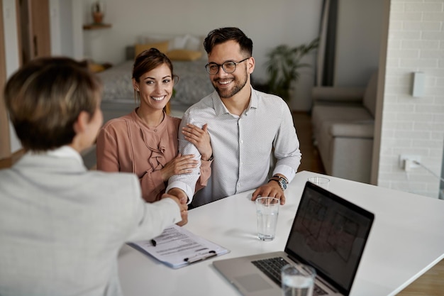 Young happy couple and real estate agent shaking hands on a meeting in the office