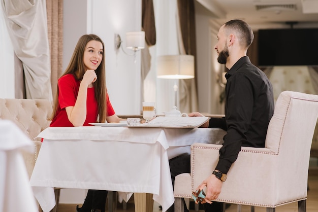 A young happy couple at the restaurant and young man hide a small box with present