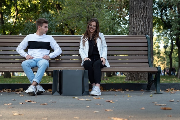 Young happy couple resting on bench. Guy and girl after successful shopping. Just married with black shopping bags.