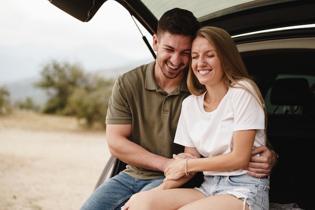 Young happy couple on a road trip sitting in car trunk