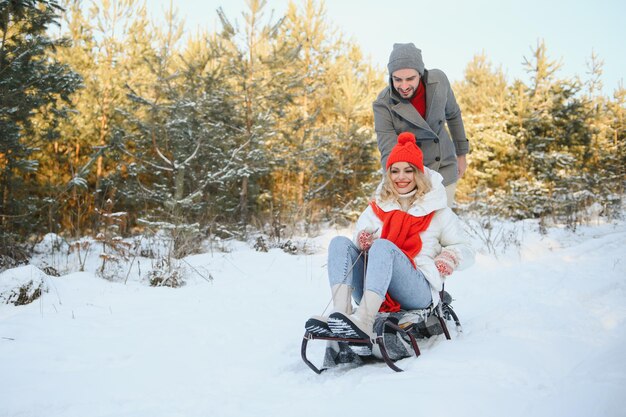 Young happy couple sledding in winter at forest