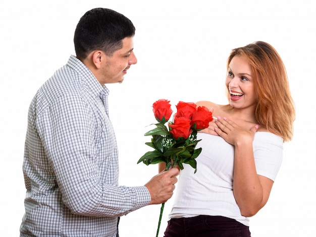 Giovani coppie felici che sorridono e nell'amore con l'uomo che dà le rose rosse e la donna che sembra sorpresa