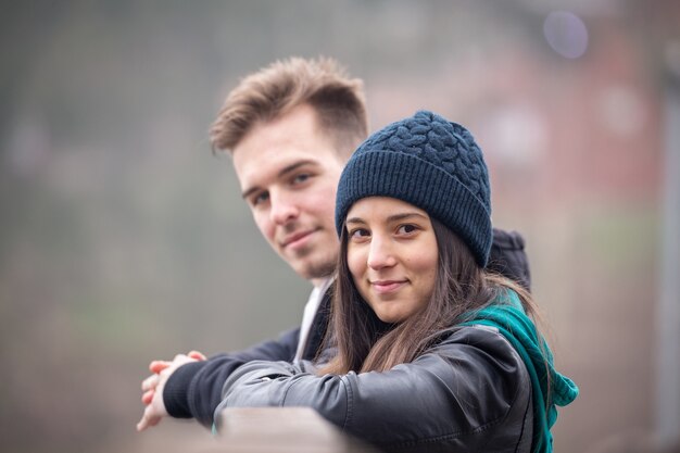 Young happy couple standing on an old wooden bridge on a foggy winter day at Lake Gebart