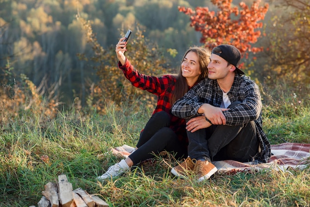 公園でスマートフォンを使用してselfieを取って幸せなカップル。