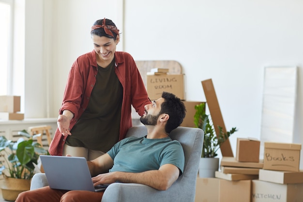 Young happy couple using laptop together while they moving to new apartment