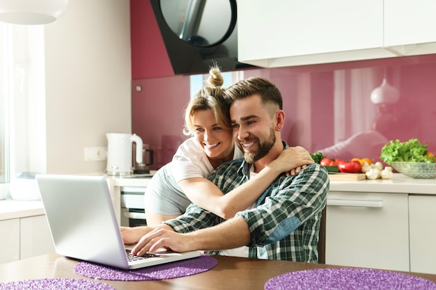 Young and happy couple using laptop for videocall in the kitchen at morning