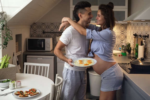 아기를 기다리는 젊고 행복한 커플. 남편과 그의 임신 한 아내는 아침 식사 시간 동안 부엌에 있습니다.