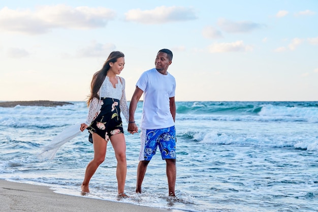 Young happy couple walking on the beach holding hands copy space