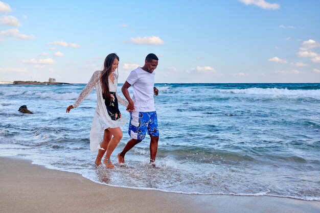 Young happy couple walking on the beach holding hands copy space