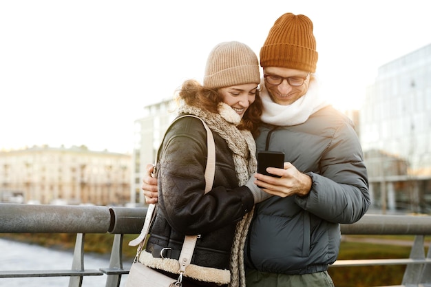 Young happy couple watching photos on mobile phone standing outdoors