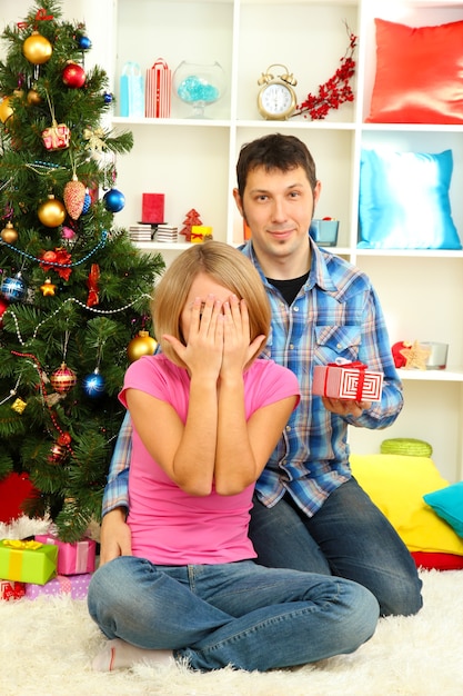 Young happy couple with presents sitting  near Christmas tree at home