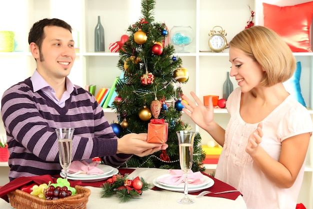 Giovane coppia felice con regali seduti a tavola vicino all'albero di natale