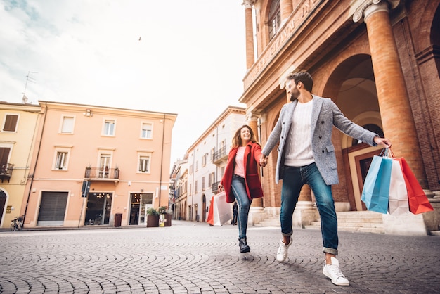 Young happy couple with shopping bags running in the city