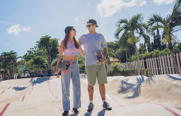 Young happy couple with skateboards enjoy longboarding at the skatepark