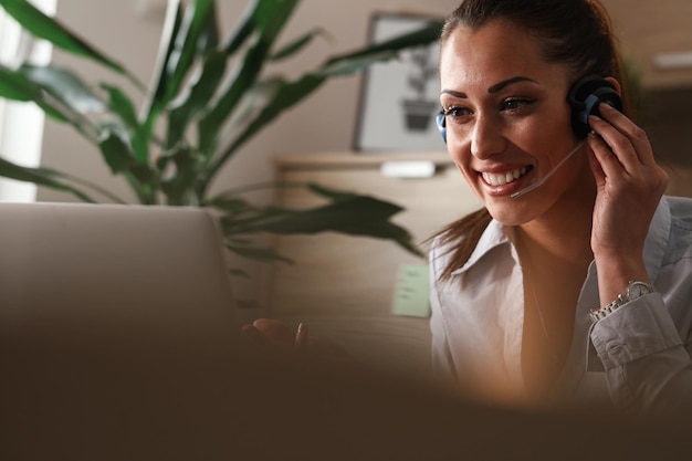 Photo young happy customer support agent with headset talking to a client while using laptop