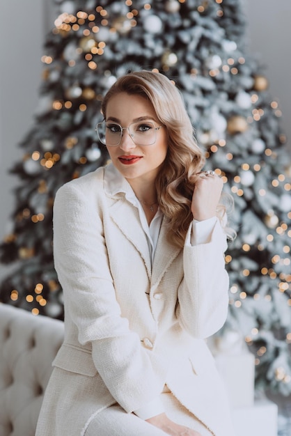 사진 겨울 방학 동안 홈 오피스에서 일하는 웃는 여성 뒤에 장식된 크리스마스 트리가 있는 직장에 앉아 안경을 쓴 젊은 행복한 유럽 사업가 소프트 선택적 포커스