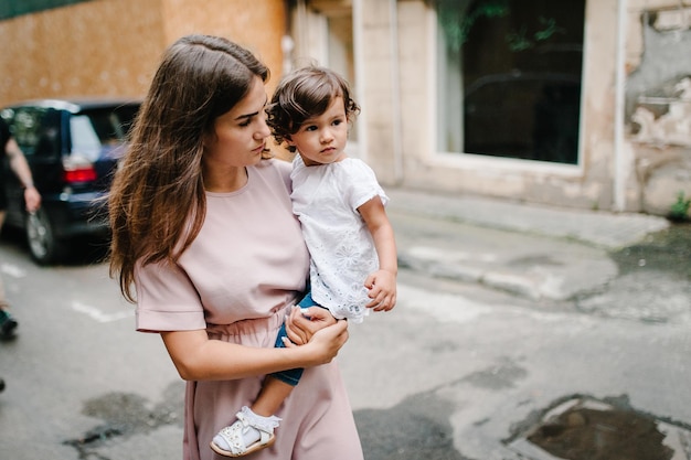 Young happy family mother and daughter during a walk the streets of the old city outdoors The concept of family holiday and travel The mom holds and hugs little girl