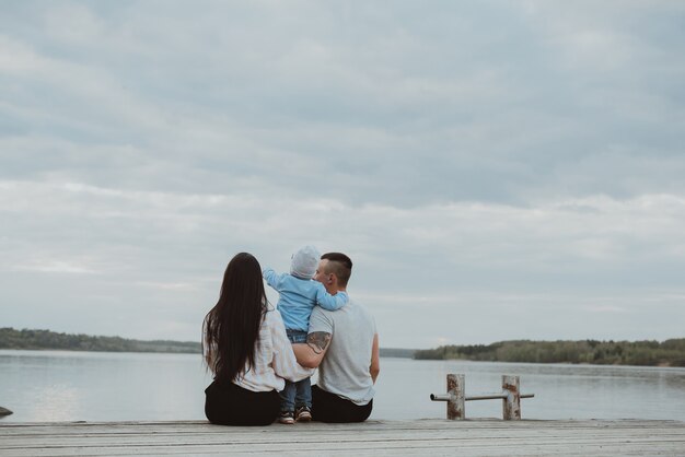 Young happy family sitting on the pier in the summer by the water